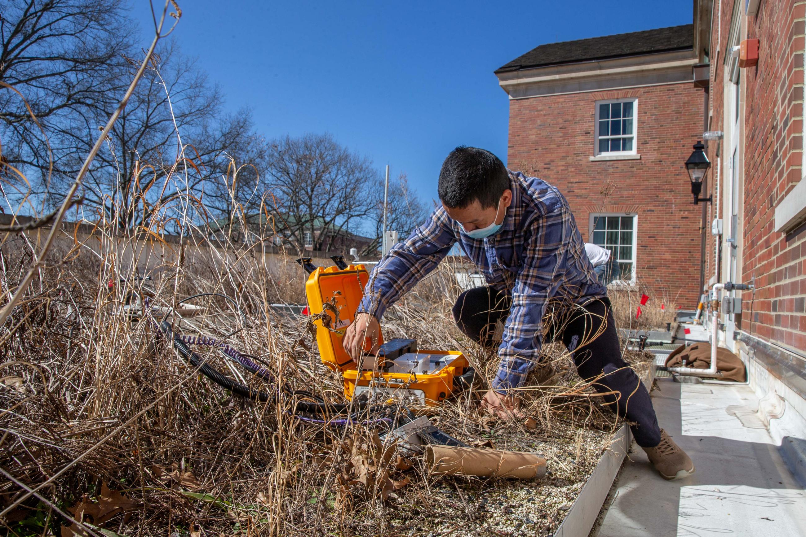 A researcher crouches in one of the planted beds on the Schoonover green roof to adjust instruments housed in a hard case.
